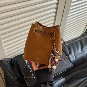 Detailansicht einer braunen Wildleder-Eimerentasche mit schickem Blumenanhänger und Gurt.