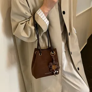 Detailaufnahme einer braunen Wildleder Eimertasche mit Metallringen und Kleeblatt Anhänger.