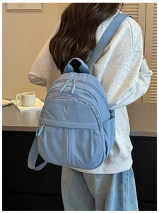 Detail shot of a light blue casual backpack worn on model, showing zipper and fabric texture.