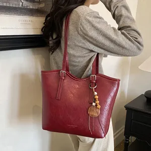 Detalle del bolso tote de cuero rojo oscuro con colgante de madera, elegante transporte al hombro.