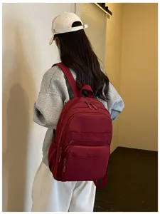 Detailed view of women casual maroon backpack with multiple zipper pockets and adjustable straps.