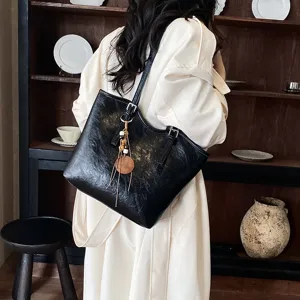 Vista detallada del elegante bolso de hombro negro con diseño de color sólido y bonitos dijes.