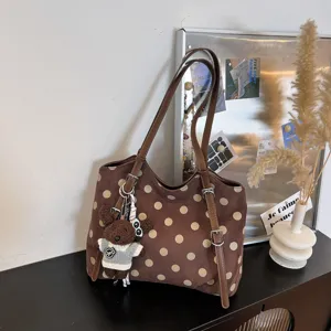 Detalle de bolso tote marrón de lunares, con correas de cuero duraderas y lindo dije de oso.