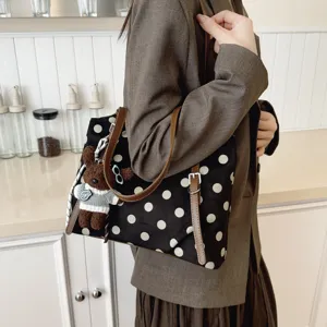 Elegante bolso tote de lona con lunares negros, correas de cuero marrón y colgante.