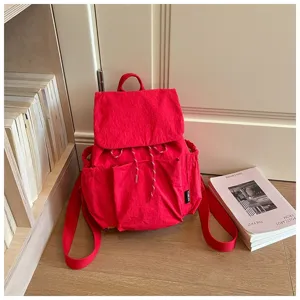 Sac à dos en tissu rouge décontracté avec cordon et multiples poches pour voyages.