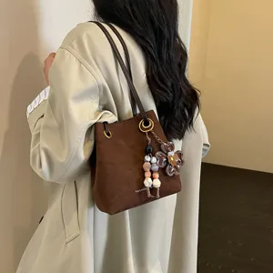 Braune Wildleder-Beuteltasche im Detail mit Blumenperlen-Anhänger und schickem Schulterriemen.