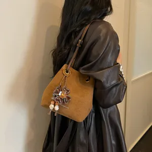 Braune Wildleder Beuteltasche Detailansicht mit Blumenanhänger und Metallring-Stil.