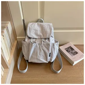 Vue détaillée du sac à dos décontracté en tissu léger gris clair, ambiance chaleureuse.