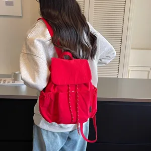 Vue détaillée d'un élégant sac à dos en tissu rouge avec fermeture à cordon et poches avant.
