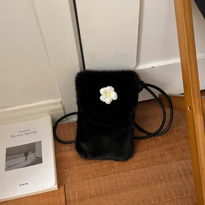 Close up view of a black plush phone bag featuring a cute knit flower on wooden floor.