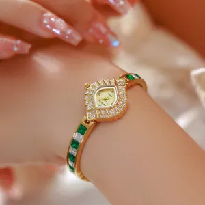 Close-up detail of luxury women watch with shield dial and green crystal bracelet.
