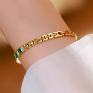 Close-up detail of women luxury retro green gemstone watch, elegant gold link bracelet strap.