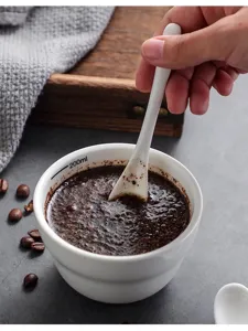 Detail view of a white ceramic coffee cupping bowl with spoon, showing capacity scale and grounds.