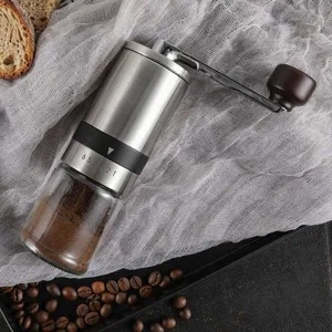 Close-up detail view of the manual coffee grinder, featuring a glass container and steel body.