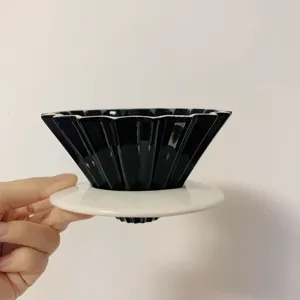 Ceramic origami coffee dripper detail view, black cone shape filter cup with white base.