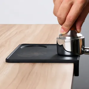 Vue de détail d'un tapis de tamper à café en silicone noir sur un bureau en bois.