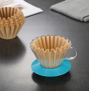 Glass coffee dripper detail view with brown filter paper and blue base on dark table.