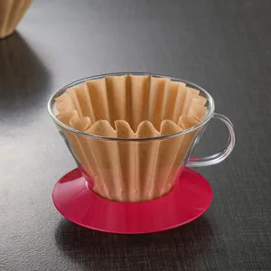 Glass pour over coffee dripper with brown paper filter and pink base on dark table main view