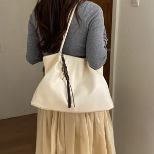 Detailed view of large capacity solid color leather tote bag with braided tassel pendant.