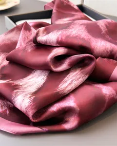 Close-up detail of luxurious wine red silk scarf featuring abstract leopard print design.