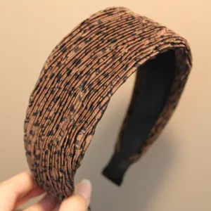 Gros plan sur le serre-tête large plissé marron avec un motif à pois sombres.