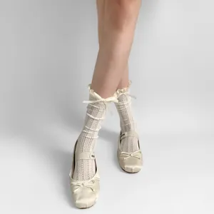 Detailaufnahme von weißen Spitzen-Rüschensocken kombiniert mit Satin-Ballett-Mary-Janes-Schuhen.