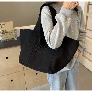 Nahaufnahme einer schwarzen Segeltuchtasche mit gesticktem Buchstaben-Design, robusteren Gurten.