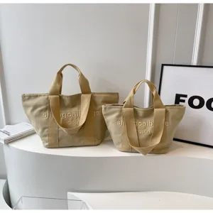Detailansicht der khakifarbenen Segeltuchtasche mit Buchstabenstickerei und stabilen Griffen.