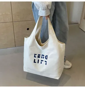 Detailansicht einer großen Canvas-Umhängetasche mit blauen Stickbuchstaben für den Alltag.