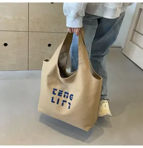 Detailaufnahme einer großen Canvas-Umhängetasche mit blauer Buchstabenstickerei für Arbeit.