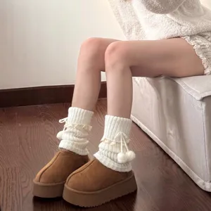 Cozy white knit leg warmers detail featuring delicate lace trim and cute pom-poms for winter style.