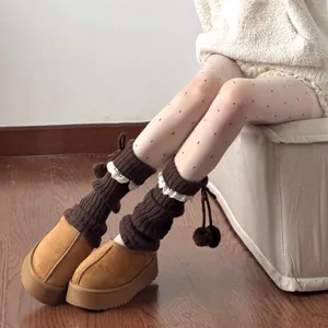 Detailed view of knitted leg warmers featuring delicate lace trim and playful pom-pom details.