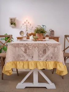Detailed view of pastoral lace crochet tablecloth with yellow gingham ruffle on table.