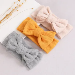 Vue détaillée de jolis bandeau pour bébé en tricot gaufré avec nœud dans des tons doux.