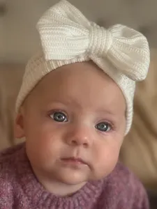 Detail shot of newborn baby white knitted bow hat, soft warm infant beanie turban headwear.