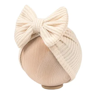 Close-up detail shot of the cute beige knitted baby hat featuring a large decorative bow on top.