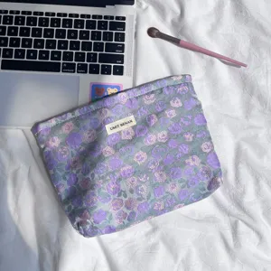 Vista dettagliata della pochette per trucco floreale viola con etichetta tessuta su fondo bianco.