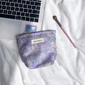 Vista dettagliata della pochette cosmetica floreale viola, con etichetta tessuta e fine tessuto.