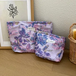 Primo piano della trousse da trucco in jacquard floreale lavanda con zip e etichetta firmata.