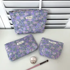Dettaglio del set di borse cosmetiche con stampa floreale viola, zip e etichetta del marchio.