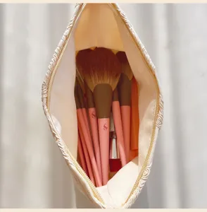 Detailed top view of large cream cosmetic bag filled with pink makeup brushes inside.