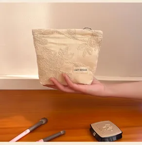 Detailed view of a beige cosmetic bag with exquisite floral embroidery and fabric brand label.