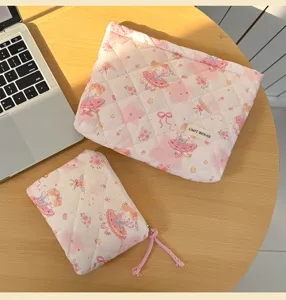Quilted pink makeup pouch set with cute cartoon print and fabric label on wooden desk detail.