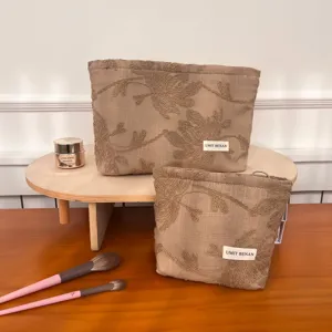 Detailed view of beige linen cosmetic bag with exquisite floral embroidery and woven brand label.
