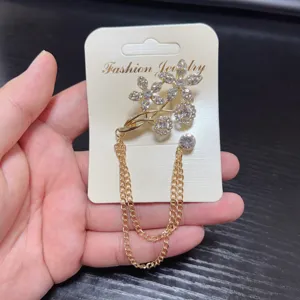 Close-up detail of a glittering rhinestone flower brooch with delicate dual gold tassel chains.