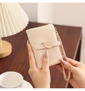 Detail shot of a minimalist beige short wallet with a chic leaf metal buckle and hand strap.