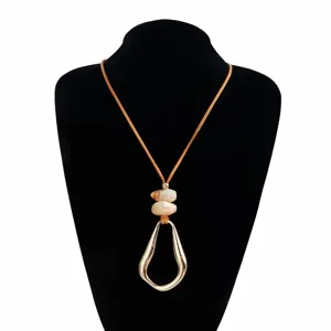 Detail view of the golden irregular hollow pendant and marbled beads on brown cord necklace.