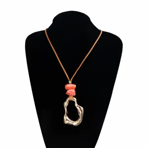 Close-up detail of the irregular hollow gold pendant and coral stone necklace on black display.
