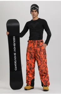 Men's orange camo waterproof cargo ski pants paired with snowboard gear in winter studio.