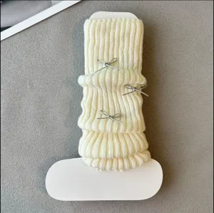 Detail view of white knitted leg warmer with cute silver bows, soft textured winter fashion accessory.
